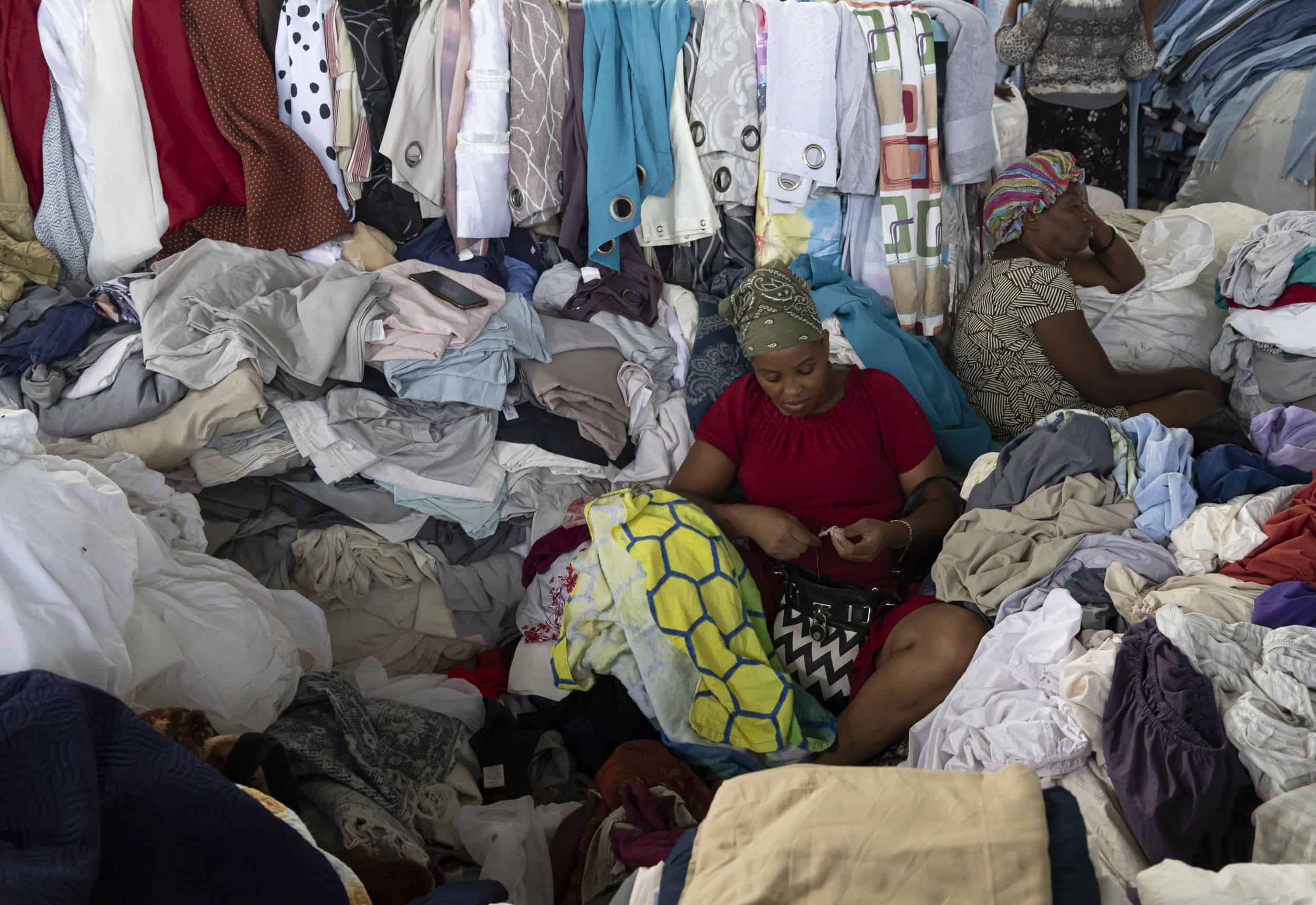 Una mujer, sentada, revisando su mercancía de telas.