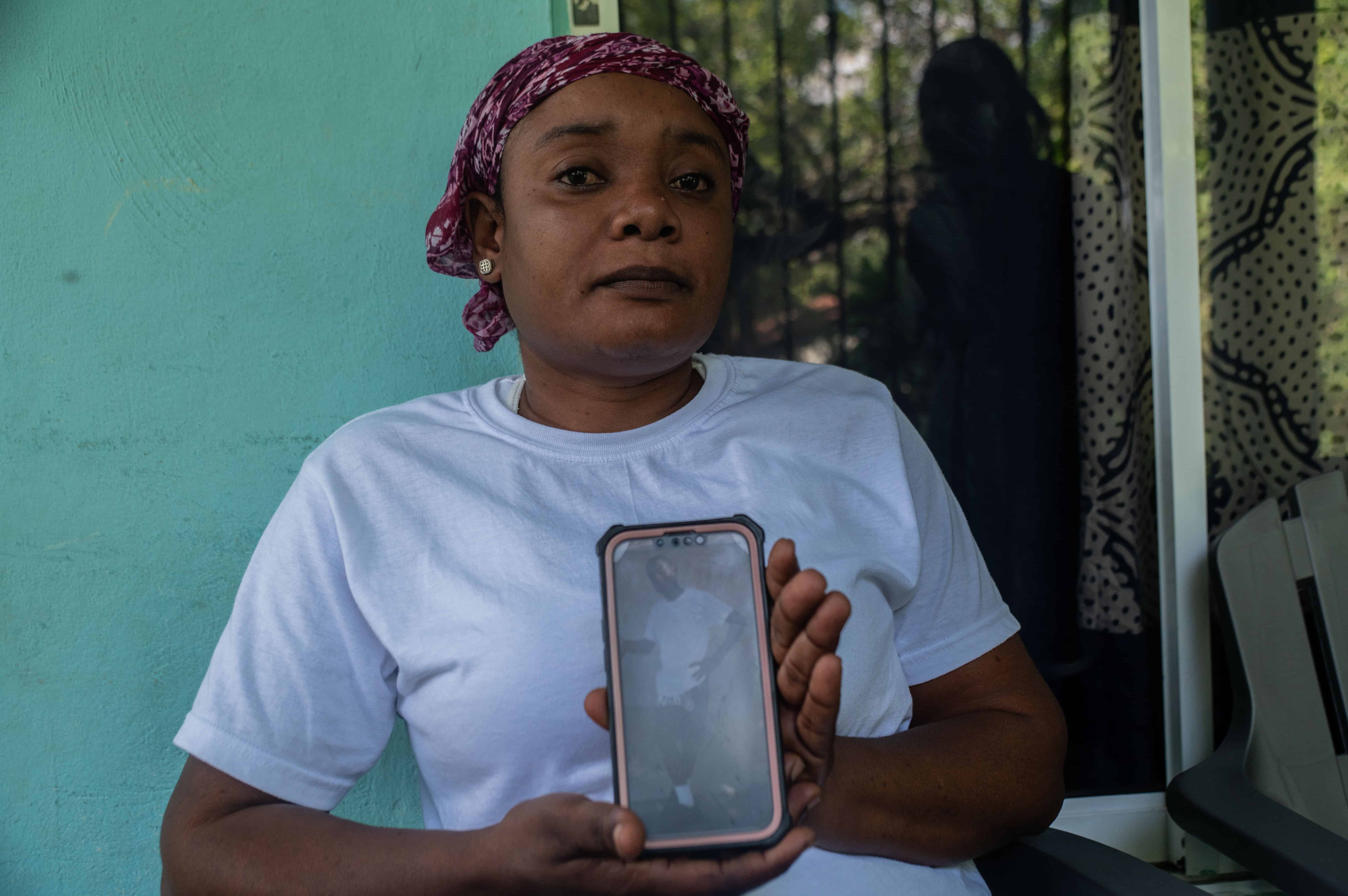 La madre de Louis Woodruch sostiene un celular con una fotografía de su hijo mientras espera la llegada de su cuerpo para velarlo. 