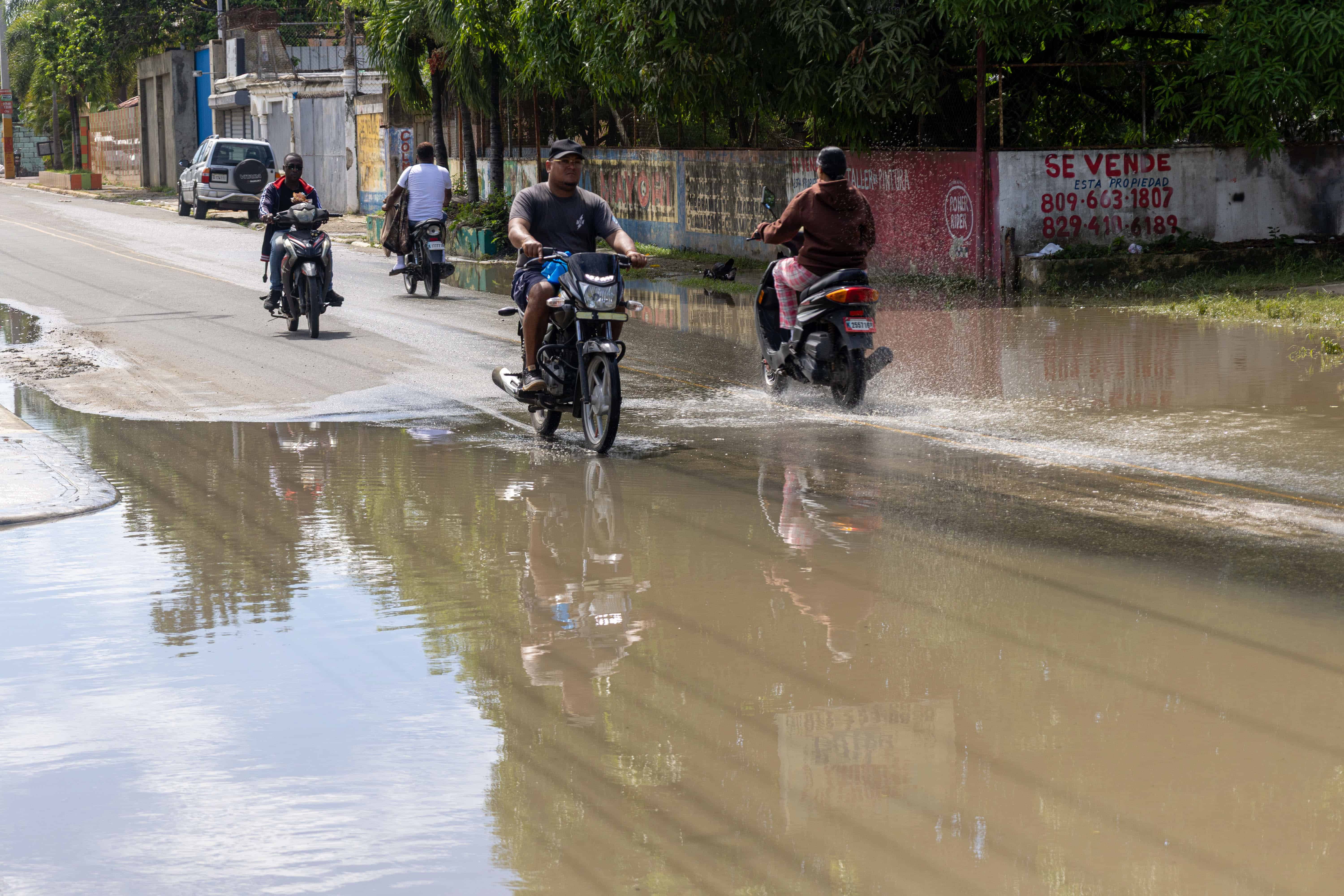 Motoristas levantaban los pies para evitar el contacto con el agua acumulada al atravesar la calle Francisco Peña Gómez, en San Luis.